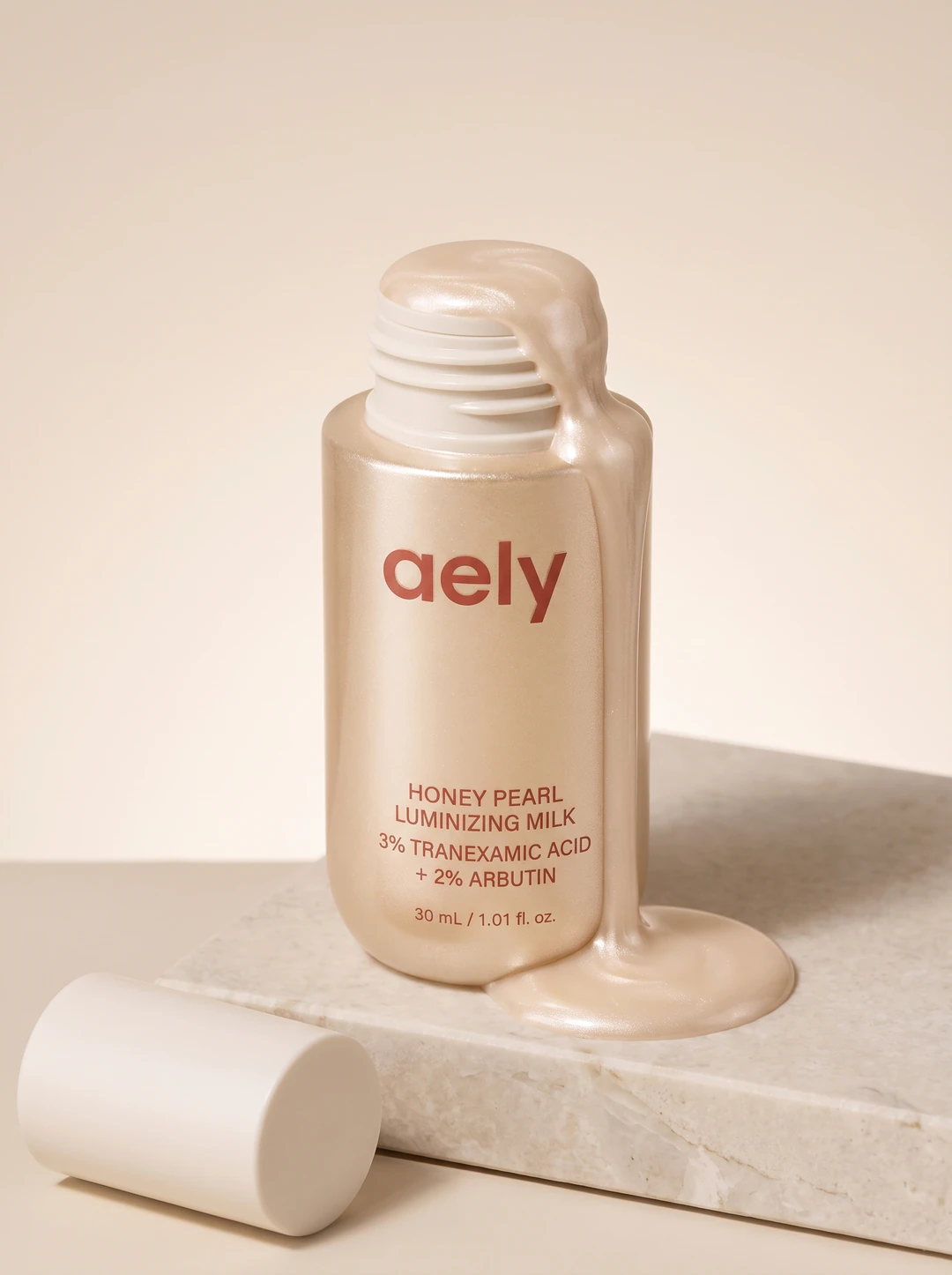 Honey Pearl Luminizing Milk, the open bottle with pearlescent milk running down one side and pooling on stone, the printed name facing out