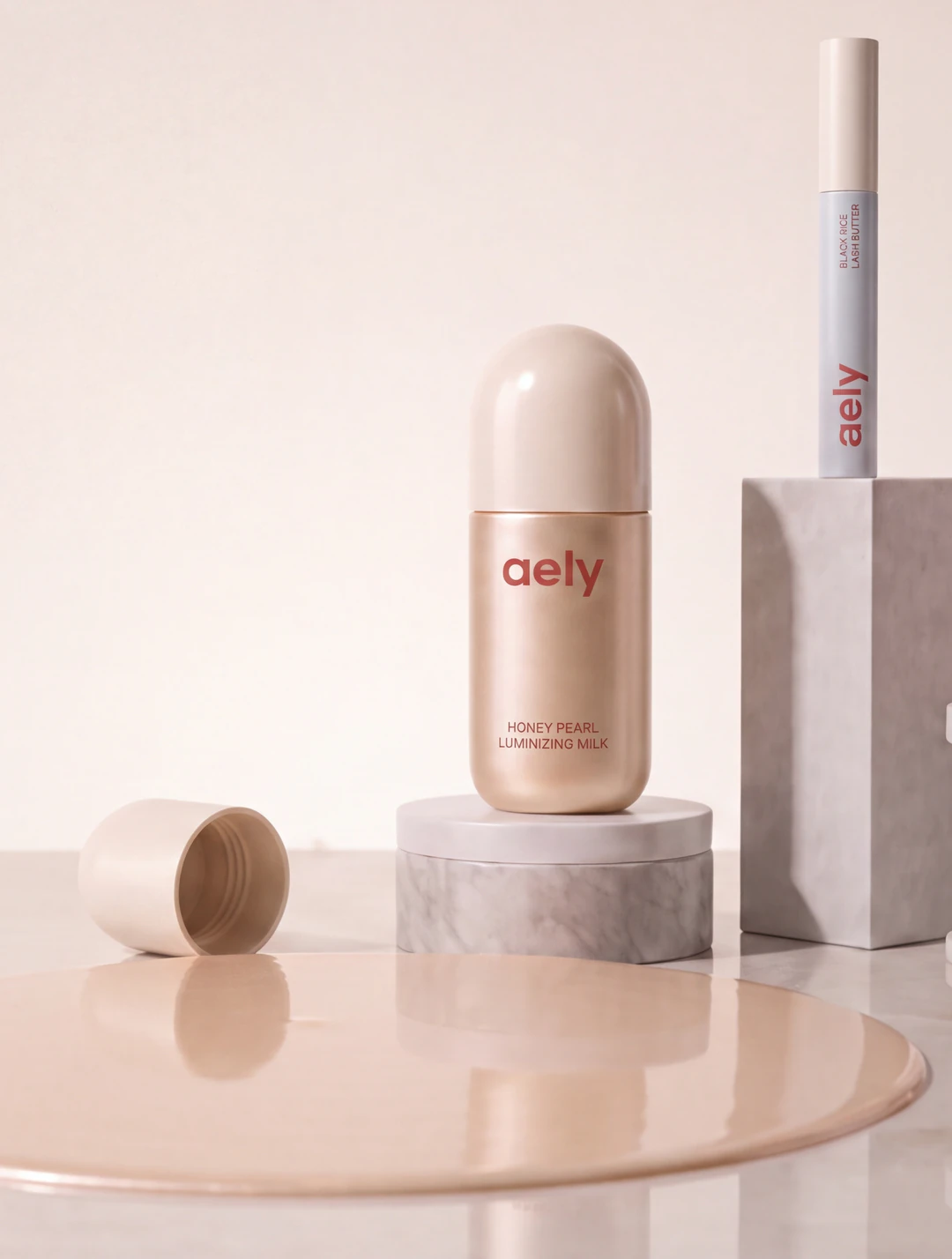 The Honey Pearl Luminizing Milk and the Black Rice Lash Butter on stone, each named on the packaging, beside a settled pool of milk
